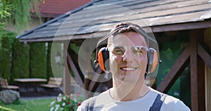 Gardener in safety glasses and headphones trimming bushes