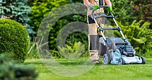 Gardener Trimming Grass Lawn Using Electric Cordless Mower photo