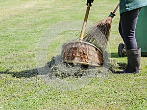 Gardener use natural broom and dust pan to sweep grass leaves after lawn trimming in green park