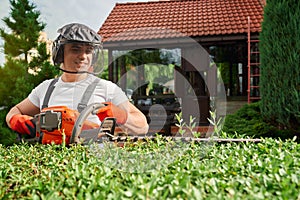 Gardener using electric hedge trimmer for shaping bushes