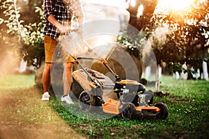 Gardener using industrial lawnmower during summer sunset. Close up details of landscaping and gardening