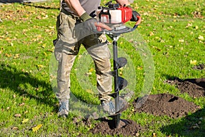 Gardener using tools hand-held soil hole drilling machine or portable manual earth auger