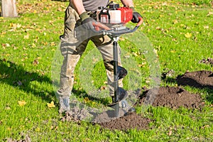 Gardener using tools hand-held soil hole drilling machine or portable manual earth auger