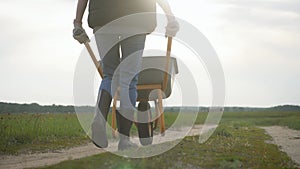 Gardener woman pushing wheelbarrow with vegetables at sunset. Silhouette of a young farmer girl in the meadow. The