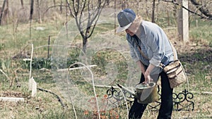 Gardener woman using watering can for watering decorative bush in garden backyard