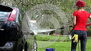 Gardener woman washing her car with strong water jet in open air.