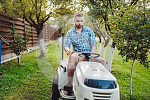 Gardener worker using lawn tractor and cutting grass through garden