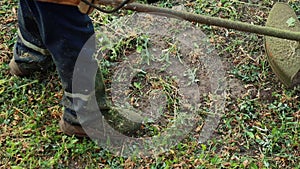 A gardener in a working uniform mows the grass with a gasoline trimmer with a fishing line in the summer, close-up. Lawn