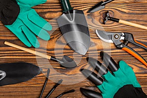 Gardening tools, pruner, gardening gloves, shovel and rake on brown wood.