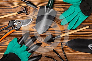 Gardening tools, pruner, gardening gloves, shovel and rake on brown wood.