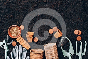 Gardening tools, seeds, pruner, rake, shovel, biodegradable pots over soil background. Spring agriculture, organic planting or
