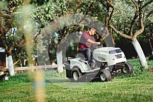 Gardening with worker using a ride on tractor, mower for cutting grass