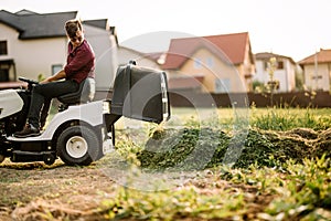Gardner using lawn tractor and cutting grass in garden during weekend time