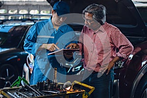 Gargae customer and car mechanic together investigate maintenance and repair programe at garage and car maintenance station