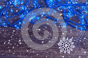 Garland with blue lights and a white snowflake on a wooden background. Christmas and New Year background.