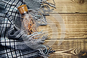 A garland of Christmas lights in a glass bottle.Warm grey scarf or plaid on a wooden background