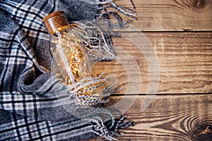 A garland of Christmas lights in a glass bottle.Warm grey scarf or plaid on a wooden background