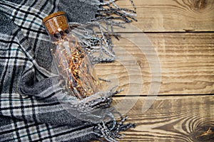 A garland of Christmas lights in a glass bottle.Warm grey scarf or plaid on a wooden background