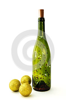 Garland in glass bottle for wine and three golden shiny christmas balls on white background. Selective focus