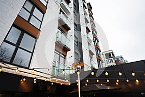 Garland of light bulbs against modern residential multistory apartment buildings. Facade of new houses