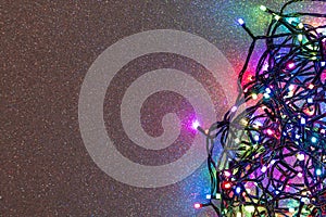 A garland of multi-colored light bulbs on a silver background with sparkles. Flat lay, top view, copy space