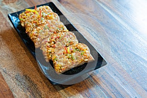 Garlic bread slices with butter mozzarella vegetable onion bell pepper on a black plate placed on a wooden table with