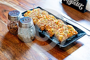 Garlic bread slices with butter mozzarella vegetable onion bell pepper on a black plate placed on a wooden table with