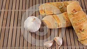 Garlic bread stuffed with cheese arranged on a bamboo mat with garlic around it on a table, selective focus