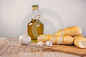 Garlic bread stuffed with cheese arranged on a cutting board with garlic around it and a bottle of olive oil on a table, selective