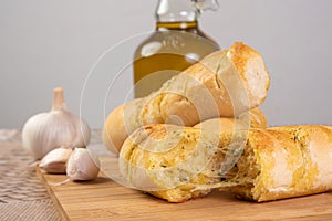 Garlic bread stuffed with cheese arranged on a cutting board with garlic around it and a bottle of olive oil on a table, selective