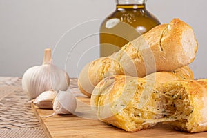 Garlic bread stuffed with cheese arranged on a cutting board with garlic around it and a bottle of olive oil on a table, selective