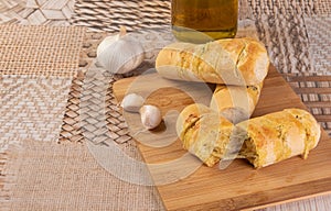 Garlic bread stuffed with cheese arranged on a cutting board with garlic around it and a bottle of olive oil on a table, selective