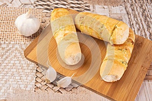 Garlic bread stuffed with cheese arranged on a cutting board with garlic around it, on a table, selective focus