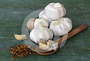 Garlic bulbs, capsules of oil extract, garlic cloves on wooden spoon