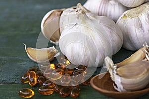 Garlic bulbs, capsules of oil extract, garlic cloves on wooden spoon