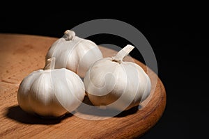 Garlic bulbs on a wooden board on a black background