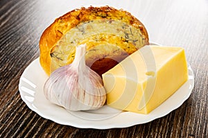 Garlic bun, piece of cheese and garlic head in plate on wooden table