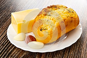 Garlic bun, piece of cheese and slices of garlic in plate on wooden table