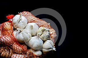 Garlic cloves and bulbs in string bag. Isolated on black background . White onions of garlic in net sack bought in greengrocer`s
