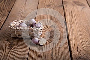 Garlic in a craft wicker basket from a vine lies on an old wooden rustic table