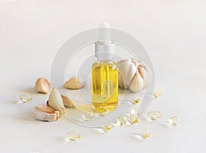 Garlic oil in a bottle and capsules near whole bulb and cloves on a white table close up
