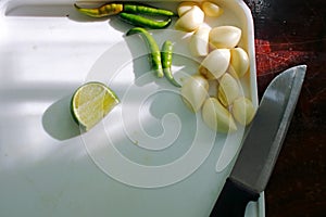 Garlic, paprika, lemon and knife on white plastic chopping board