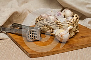 Garlic solo in a wicker basket on a wooden Board on a linen background. next to the knife, press