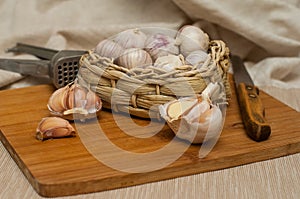 Garlic solo in a wicker basket on a wooden Board on a linen background. next to the knife, press