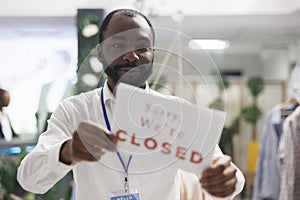 Garment department store african american employee hanging closed sign