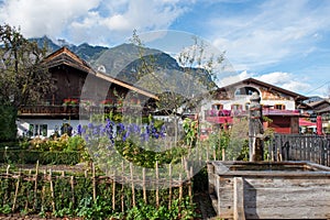 Garmisch-Partenkirchen, old water well, alpin houses, wooden balcony, blooming flowers in summer garden,  mountains, Upper Bavaria