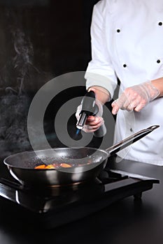 Gas burner in the hands of the chef. Cooking flamb dishes from berries and fruits.Flaming of fruits and berries on fire