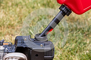 Gas can pouring gasoline into fuel tank of lawnmower