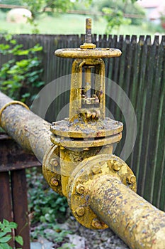 Gas pipe with big old valve-crane. Industrial gas pipeline laid along fence, gasification of population