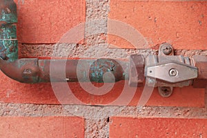 Gas pipes and a valve against a red brick wall